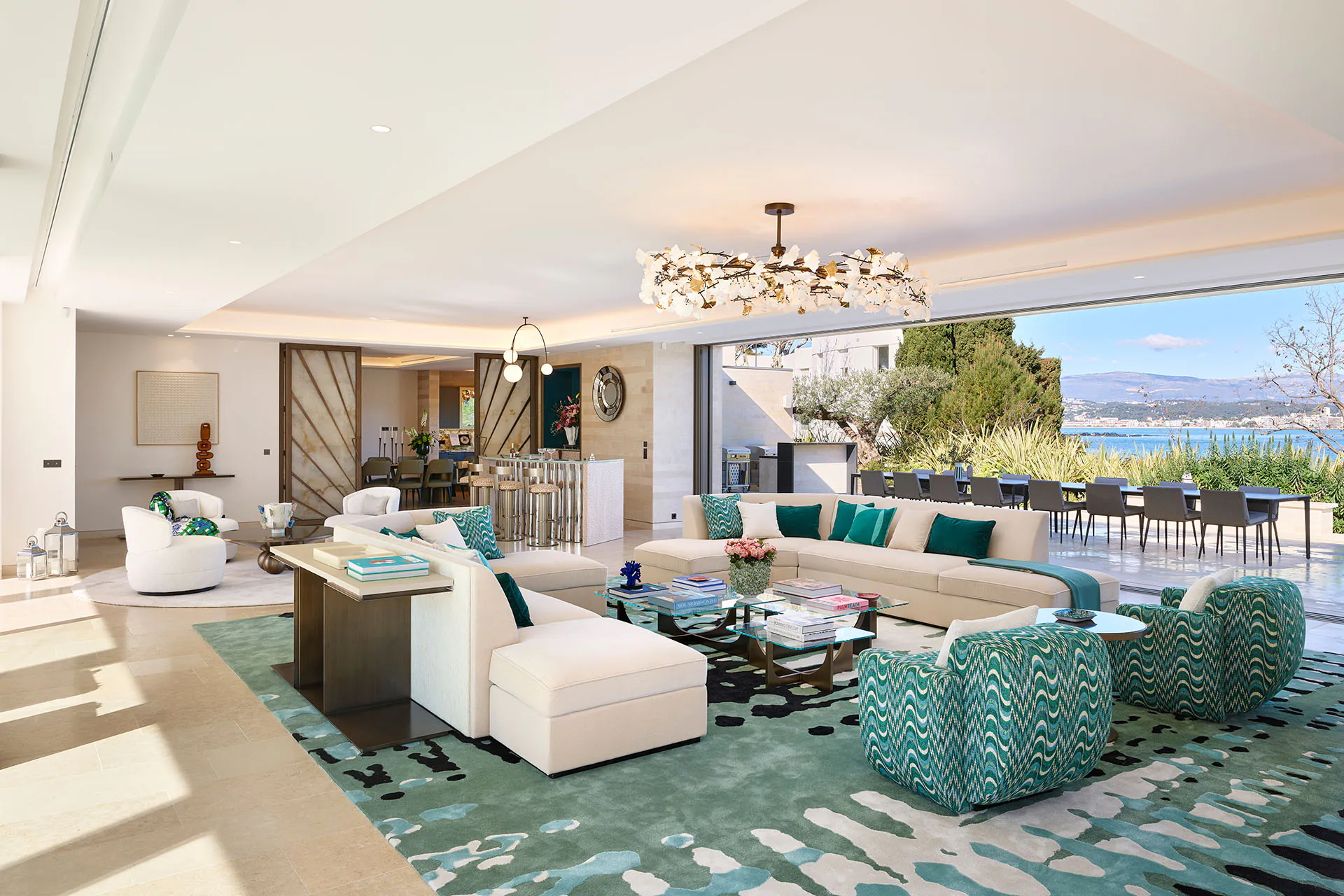 Open-plan reception room at Domaine de la Belle Étoile with cream sofas, teal accents, floral chandelier and sea views
