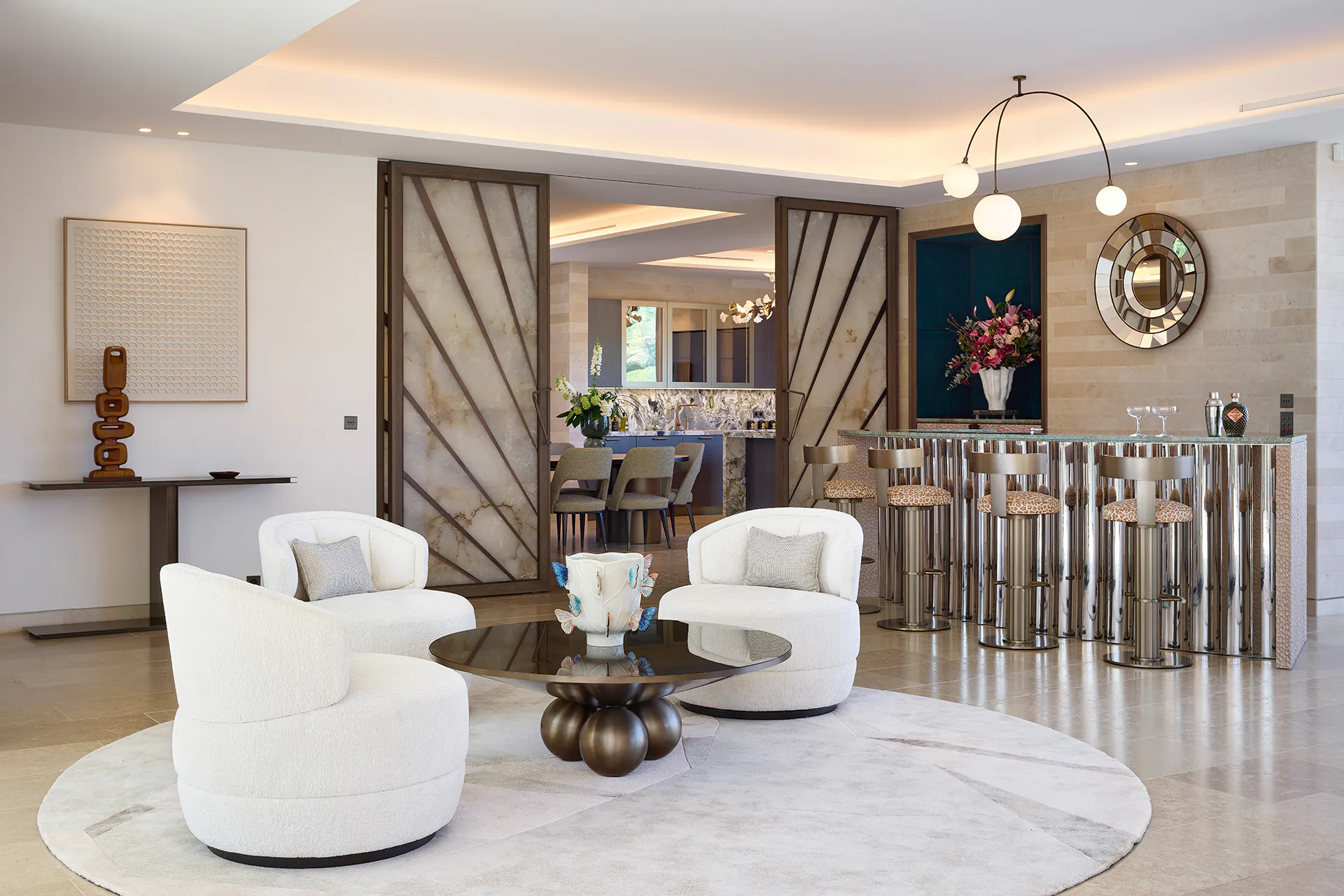 Villa reception room at Domaine de la Belle Étoile with white bouclé armchairs, chrome bar, marble pivot doors and sculptural coffee table