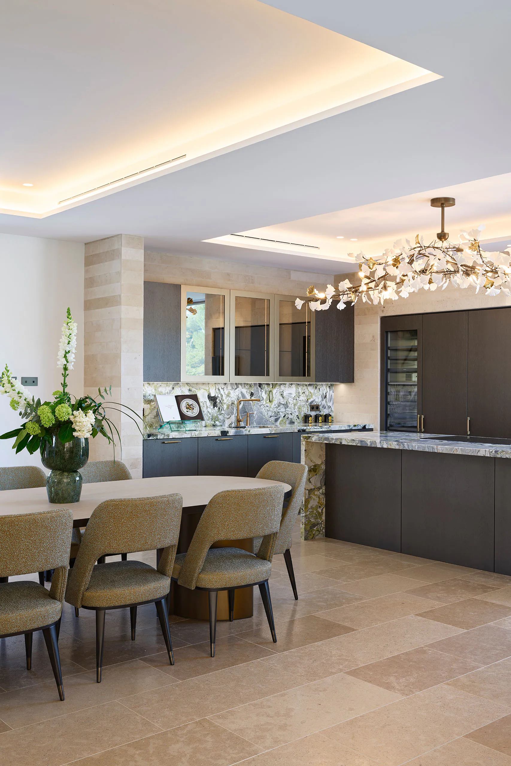 Luxury kitchen at Domaine de la Belle Étoile with dark cabinetry, marble island, oval dining table and floral chandelier
